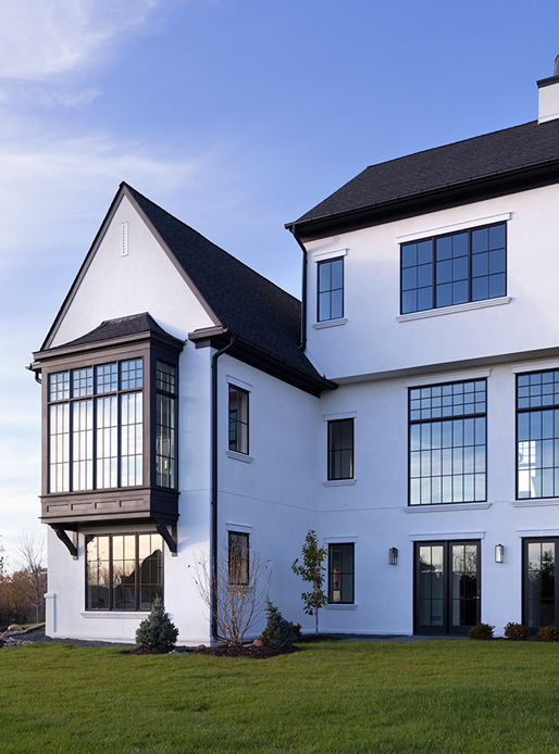 Large white home with black windows featuring large bay window off the back